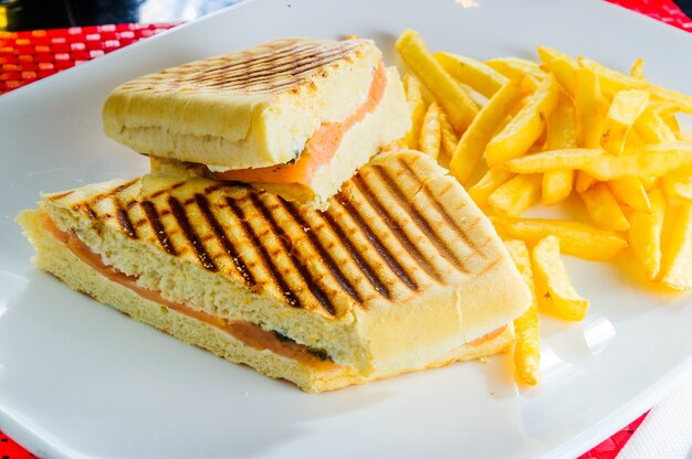 Club sándwich a la parrilla con papas fritas aislado en un plato blanco.