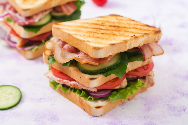 Club sandwich con pechuga de pollo, tocino, tomate, pepino y hierbas.