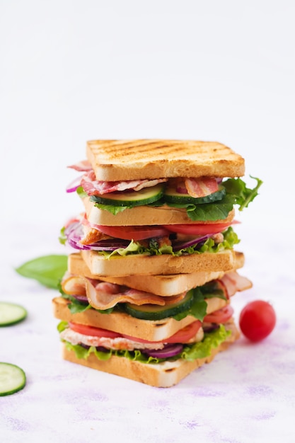 Club sandwich con pechuga de pollo, tocino, tomate, pepino y hierbas.