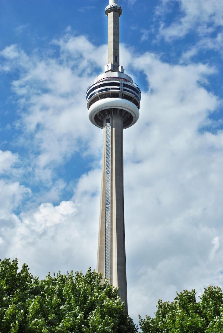 CN Tower gegen blauen Himmel mit Wolken aus einem Park in der Innenstadt von Toronto, Kanada.
