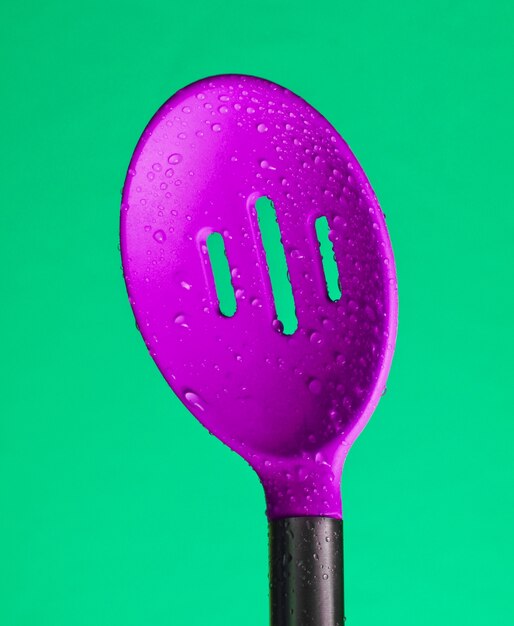 Coador de silicone para colher de cozinha em gotas de água sobre fundo verde