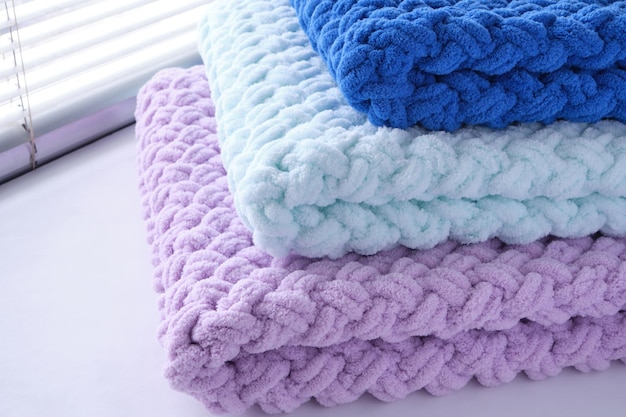 Cobertores de bebê artesanais quentes, delicados e macios em três cores de azul, lilás e menta no fundo da janela.