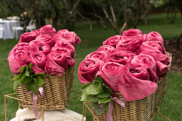 Cobertores rosa quentes enrolados em forma de rosas em uma grande cesta para convidados em uma festa de casamento ao ar livre