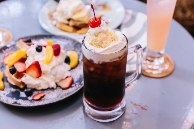 Cobertura de refrescamento doce da cereja da cola com uma colher do gelado de baunilha e da cereja fresca.