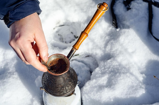 Cobre cezve haciendo café en la naturaleza bosque nevado la mano del hombre mezcla café con una cuchara