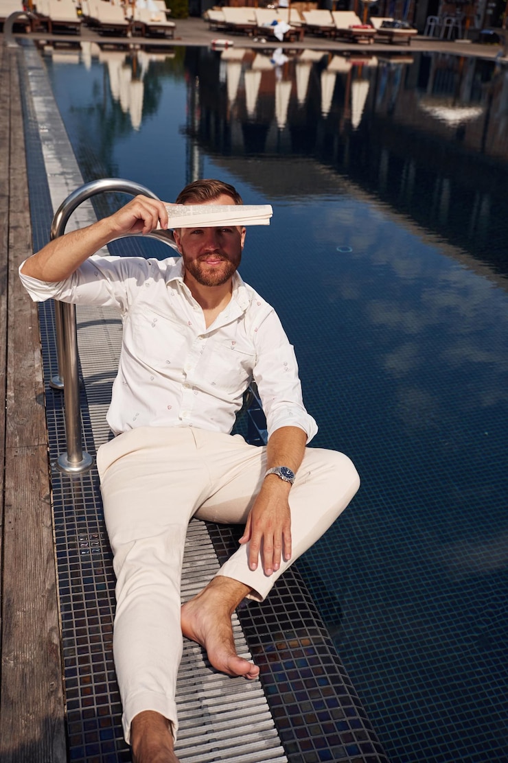 Foto cobrindo-se com jornal da luz do sol brilhante um homem bonito em roupas formais está na piscina