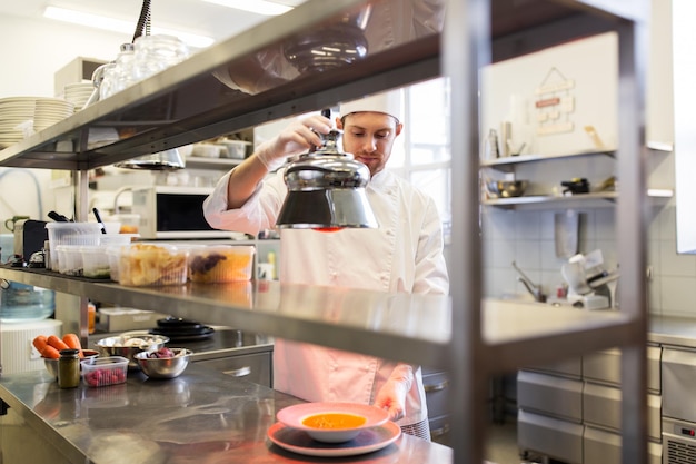 Foto cocción de alimentos, profesión y concepto de la gente - cocinero masculino feliz calentando sopa en cloche sirviendo plato con lámpara en la cocina del restaurante