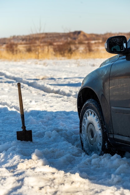 Coche atascado en la nieve fuera de la carretera a la luz del día con pala y enfoque selectivo