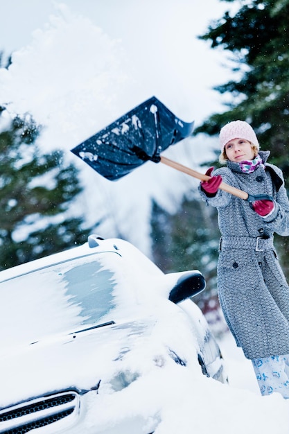 Foto coche atascado en la nieve y una mujer paleando