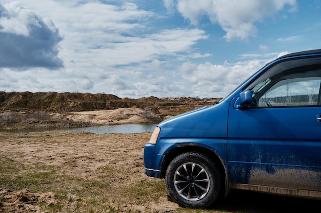 Un coche azul está acampando en el claro sobre el fondo de las dunas de arena y el cielo azul con nubes en un día soleado