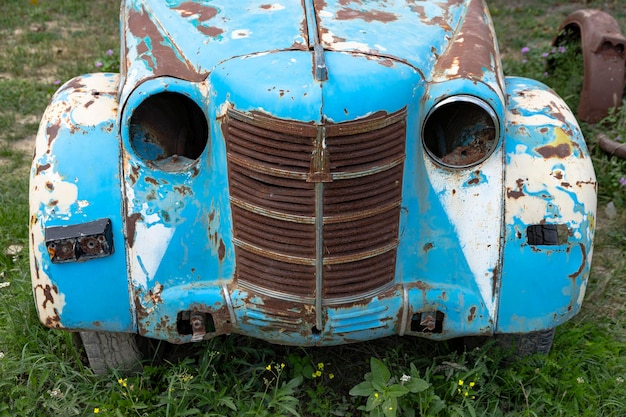 Coche azul oxidado vintage en la calle con hierba verde