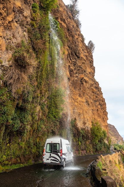 Un coche bañándose en la cascada que cae sobre la carretera llamada Cascada Anjos Madeira Portugal