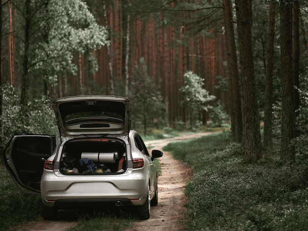 Coche con un baúl abierto lleno de cosas para acampar Concepto de tiempo familiar al aire libre en el bosque Vehículo europeo moderno desde atrás en el bosque