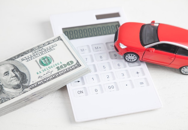 Foto coche, calculadora y dinero sobre fondo blanco.