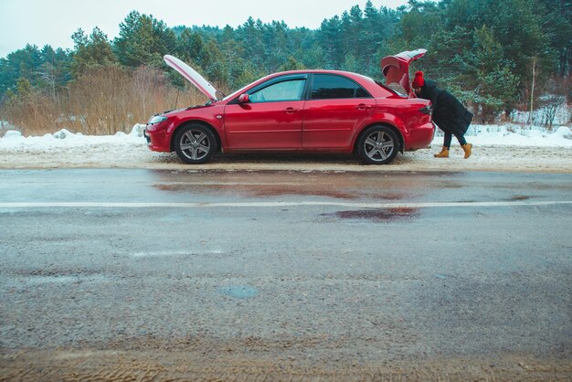 Coche con capota abierta mujer mirando en el maletero avería en la carretera temporada de invierno