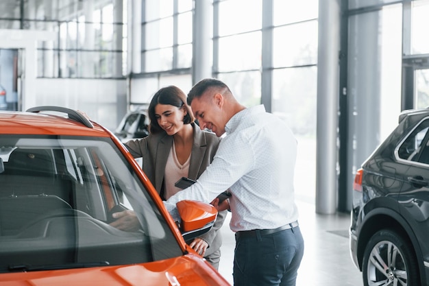 Foto coche de color naranja hombre con ropa formal que ayuda al cliente con la elección del automóvil