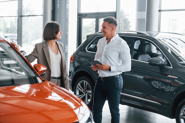 Coche de color naranja Hombre con ropa formal que ayuda al cliente con la elección del automóvil