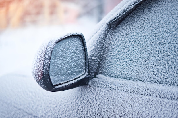 Coche cubierto de nieve estacionado afuera Primer plano del espejo retrovisor congelado