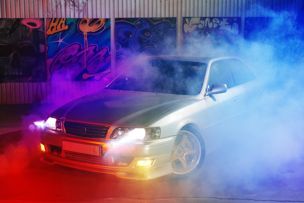 Coche deportivo en la calle de la ciudad nocturna a la luz de neón con humo