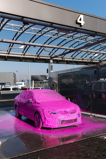 Coche deportivo de lujo azul en autoservicio lavado de coches espuma rosa en cierre automático