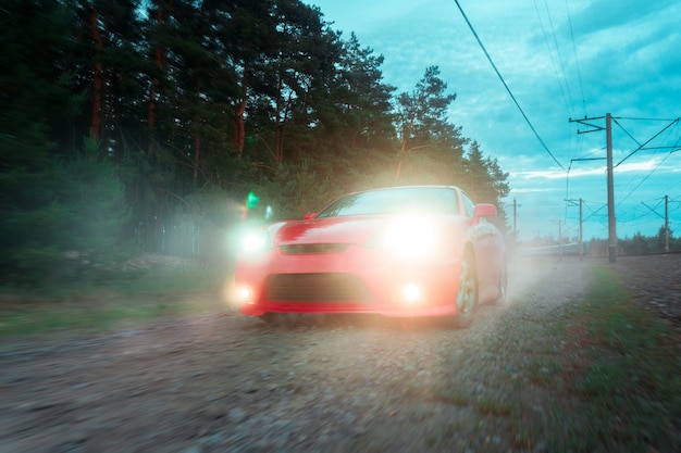 Coche deportivo rojo se mueve sobre terreno accidentado con faros