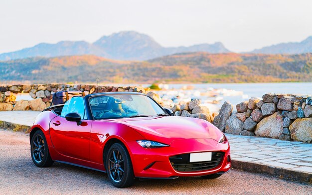 Foto coche descapotable rojo en la carretera de porto rotondo en costa smeralda en la isla de cerdeña en verano de italia. transporte conduciendo por la autopista de europa. ver en la autopista. provincia de olbia. técnica mixta.