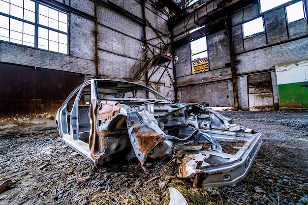 Coche en descomposición en fábrica abandonada Interior de una fábrica abandonada con maquinaria vieja