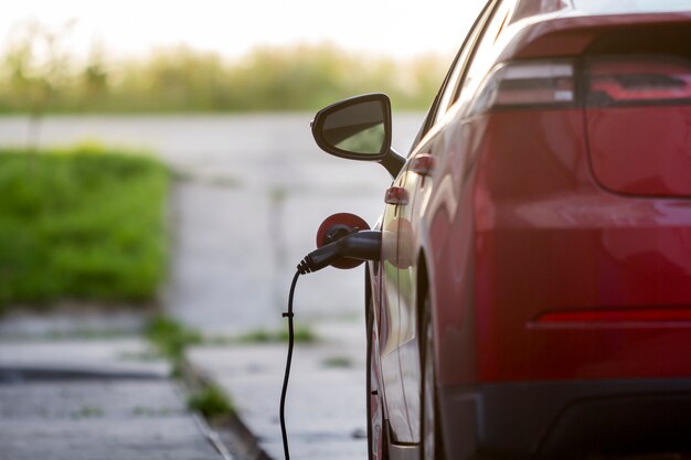 Coche eléctrico que se recarga en la calle soleada brillante. Cable del cargador enchufado al enchufe. Concepto de tecnología moderna.