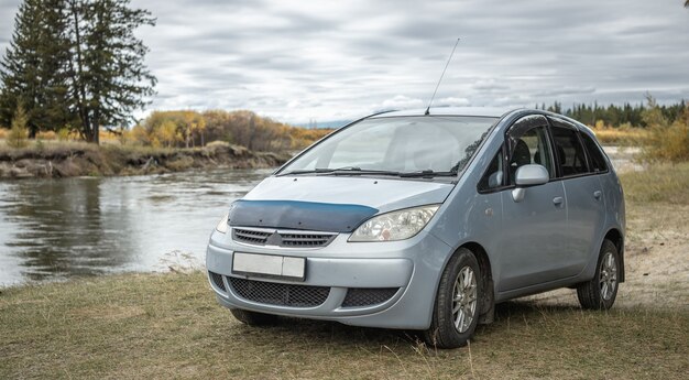 El coche está aparcado en la orilla de un río rápido junto a un bosque otoñal de color verde amarillo. Concepto de viaje, naturaleza hermosa y estado de ánimo otoñal