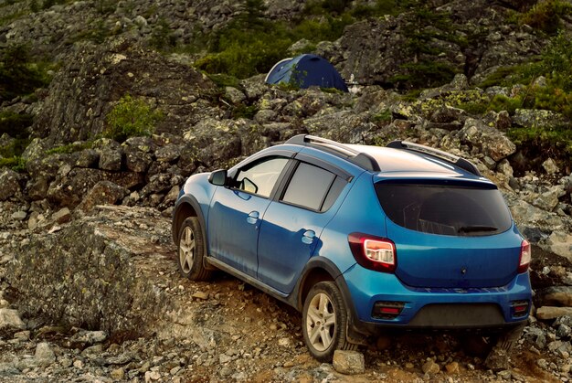 El coche está aparcado entre las rocas en primer plano, la carpa en el fondo es visible