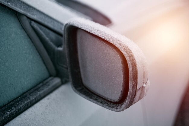 Coche estacionado afuera durante la temporada de invierno La foto macro de un espejo retrovisor lateral está cubierta con una fina capa de hielo Mañana helada