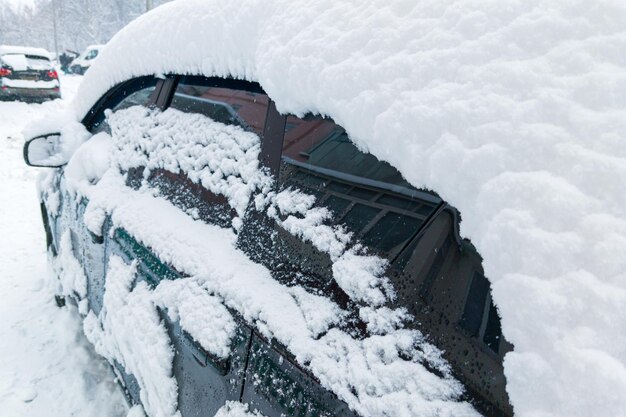 Coche estacionado cubierto por una gruesa capa de nieve después del primer plano de la ventisca de invierno con enfoque selectivo