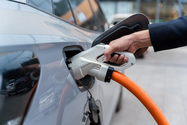 Coche EV Mano de un hombre que sostiene la carga del coche eléctrico se conecta al coche eléctrico en la estación de carga del coche eléctrico Concepto de energía verde y reduce las emisiones de CO2