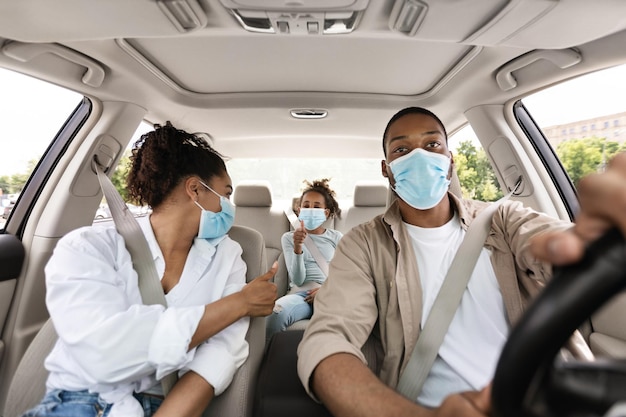 Foto coche de familia negro con máscaras faciales gesticulando con los pulgares hacia arriba