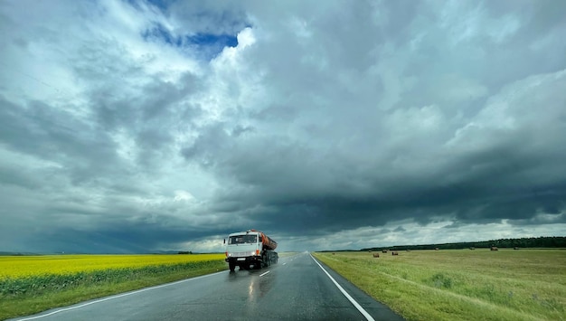 Coche grande moviéndose por la carretera mojada después de la lluvia. Campo amarillo y cielo nublado alrededor. Viajar en coche con