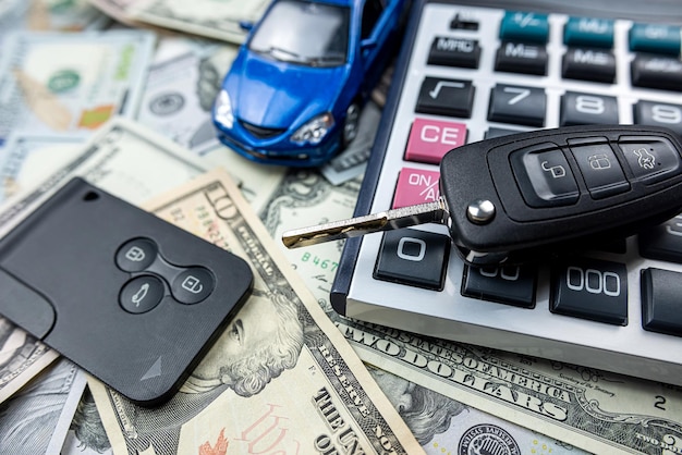 Foto coche de juguete azul con calculadora de llaves reales sobre billetes de dólar estadounidense