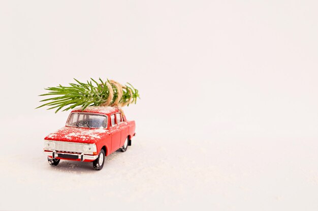 Coche de juguete de entrega de árbol de Navidad retro rojo sobre un fondo blanco en invierno con nieve