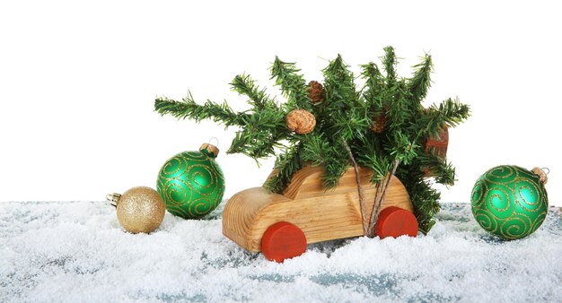 Coche de juguete de madera con árbol de Navidad y adornos sobre una mesa nevada sobre fondo blanco.