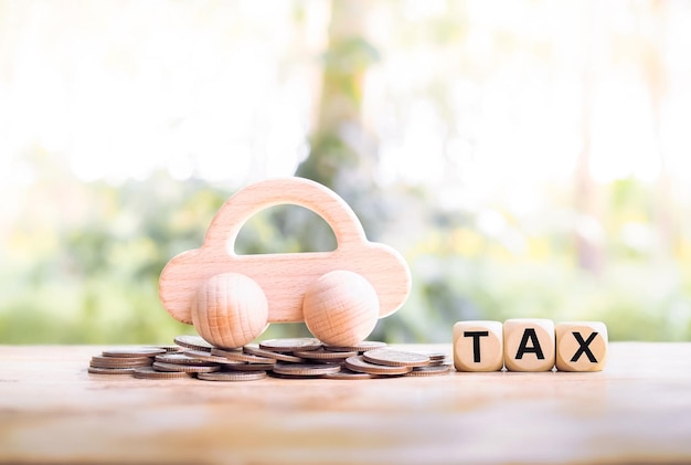 Coche de juguete de madera sobre una pila de monedas y bloques de madera con la palabra IMPUESTO El concepto de pagar impuestos por coche