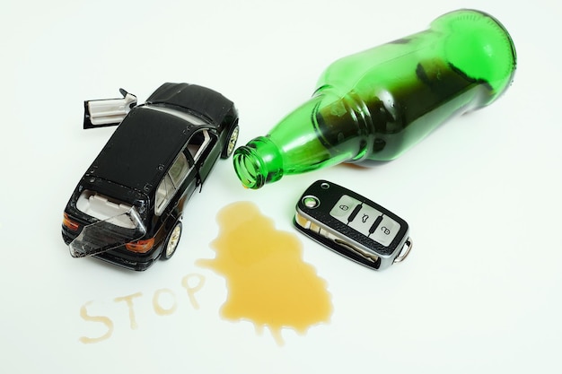 Foto un coche de juguete roto una botella con restos de alcohol y una llave de coche sobre un fondo blanco.