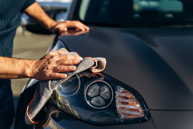 Coche de limpieza con paño de microfibra. Vista recortada del hombre caucásico limpiando su coche en la calle. Concepto de coche pulido de hombre