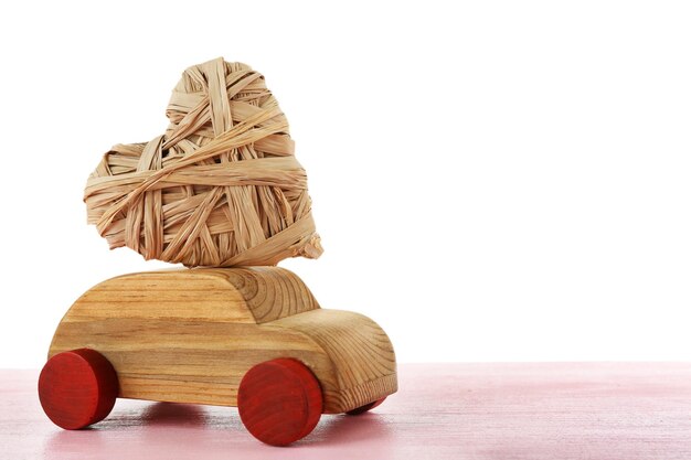 Coche de madera con un corazón de mimbre en una mesa de madera rosa