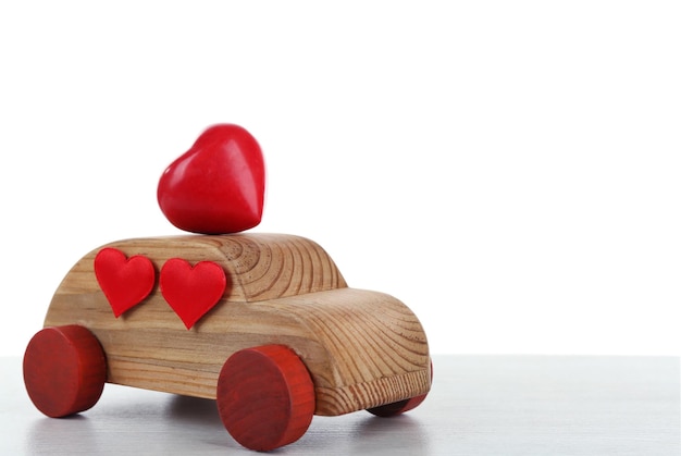 Coche de madera con corazoncitos rojos sobre una mesa de madera blanca