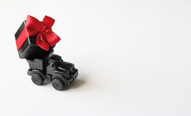 Coche negro con un regalo y un lazo rojo sobre un fondo blanco, preparación de primer plano para las vacaciones
