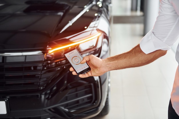 Coche negro Vista de cerca de la mano del hombre que sostiene el teléfono con etiquetas e íconos Concepción del control remoto