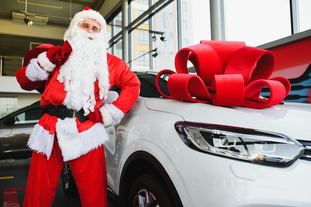 Coche nuevo como regalo de Navidad. Santa Claus en la sala de exposición de automóviles cerca de un automóvil nuevo.