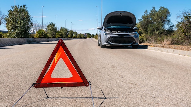 Coche con problemas y un triángulo rojo para advertir a otros usuarios de la vía Un coche averiado