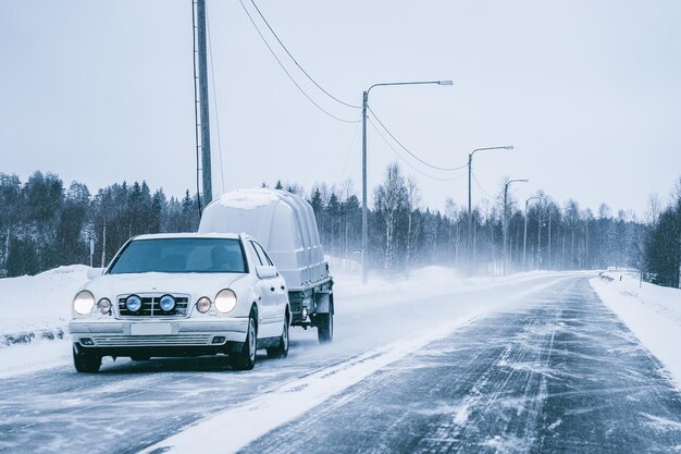 Coche con remolque en el camino nevado de invierno en Rovaniemi en Laponia, Finlandia