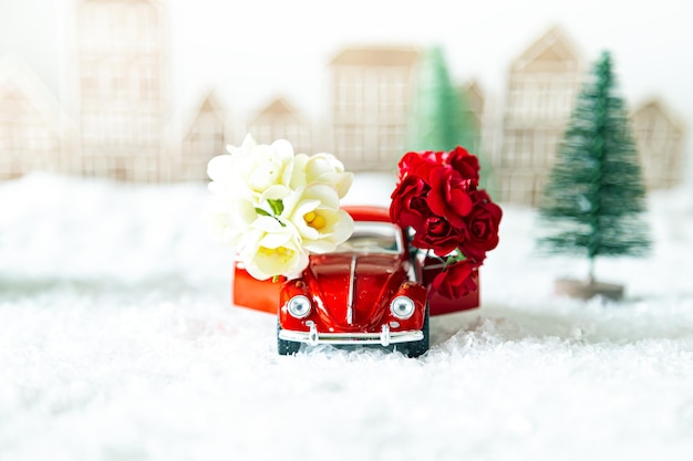 Coche retro rojo con flores en un paisaje invernal. Postal para el Día de la Madre o el Día de los Enamorados. Entrega de flores para las vacaciones. Enfoque selectivo.