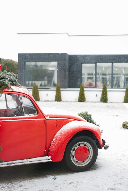 Un coche rojo con un árbol de Navidad se encuentra en la calle cerca de la casa.